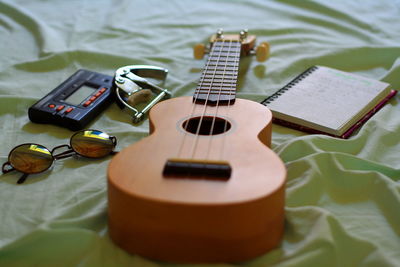 Close-up of ukulele by sunglasses on bed