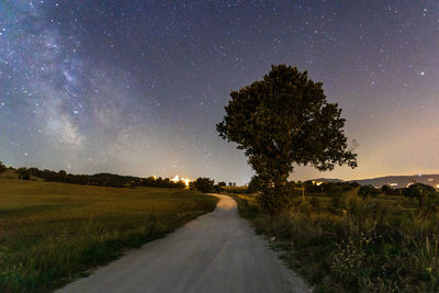 Road amidst trees on field against sky at night