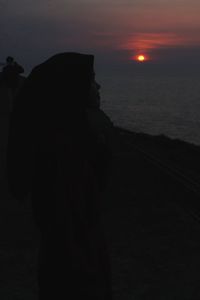 Silhouette woman standing on beach against sky during sunset