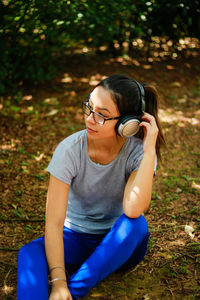 High angle view of young woman listening music while sitting on field in park