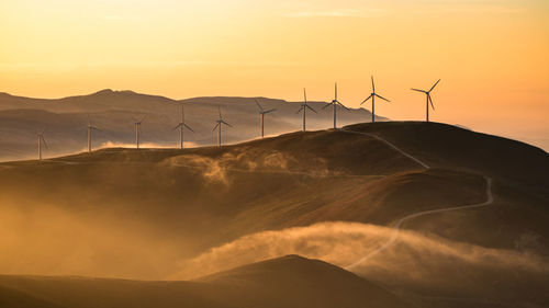 Low angle view of silhouette windmills on mountain against sky during sunset