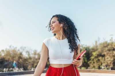 Smiling woman listening to music through in-ear headphones at skate park