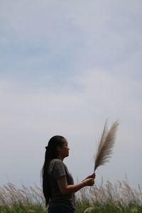 Side view of woman holding pampas grass while standing on field against sky