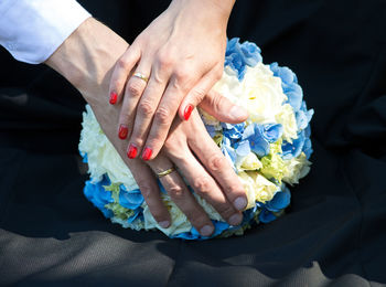 Cropped hands of bride and bridegroom touching bouquet on table