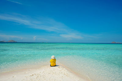 Rear view of woman sitting on beach against blue sky