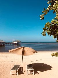 Chairs and parasol at beach against blue sky