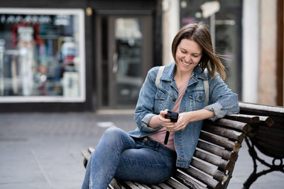 Smiling young woman using camera while sitting on bench