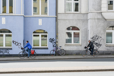 Side view of men riding bicycles on road against building