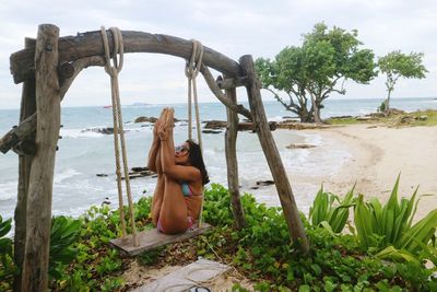 Mid adult woman stretching leg on swing at beach