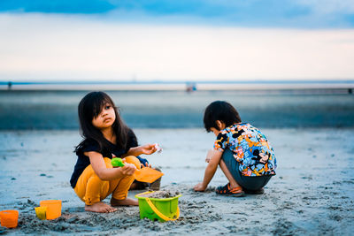 Women sitting on shore at beach against sky