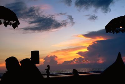 Silhouette people at beach against sky during sunset