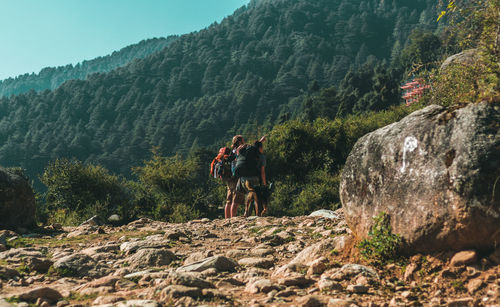 Rear view of men on rock by mountains against sky