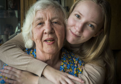 Close-up portrait of granddaughter embracing grandmother while at home