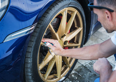 Cropped image of man cleaning car wheel outdoors