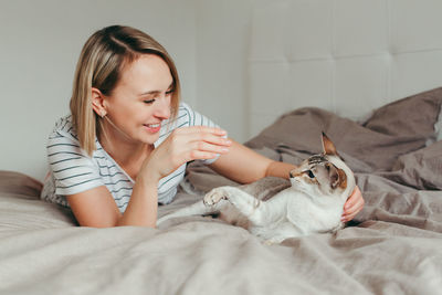 Young woman playing with cat on bed