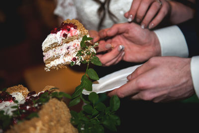 Cropped hands of bride and bridegroom holding wedding cake