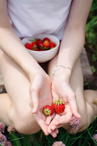 A teenage girl with a bowl of strawberries in her hands sits on a bed in the garden vertical view