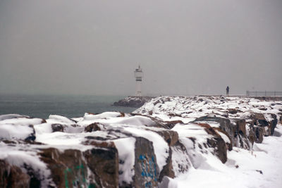 Lighthouse by sea against sky during winter