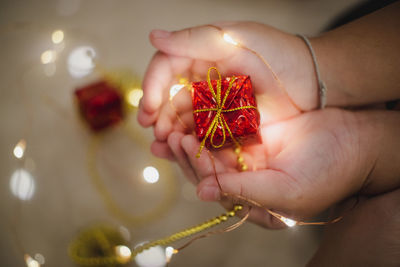 Cropped hands of person holding small gift with illuminated string lights