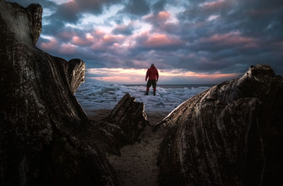 People standing on rock by sea against sky during sunset