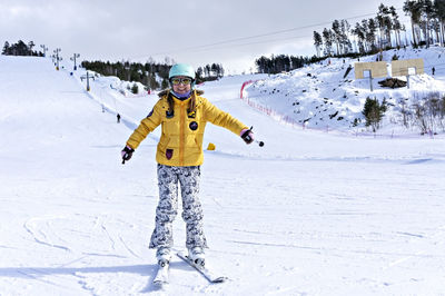 Happy young woman in yellow jacket ski helmet skiing on mountain slope, winter sports alpine skiing 