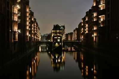 Illuminated buildings by river against sky in city at night