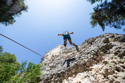 Low angle view of male friends climbing on mountain against clear blue sky