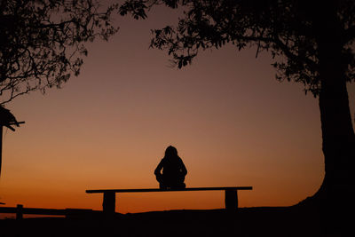 Silhouette woman sitting on bench against sky during sunset