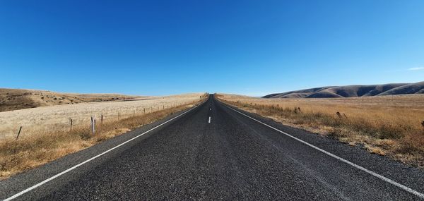 Road amidst land against clear blue sky