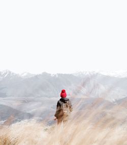 Rear view of mature man with backpack walking on mountain against clear sky