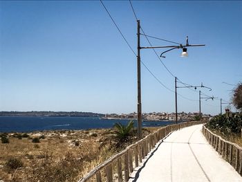 Electricity pylon on road by sea against clear sky