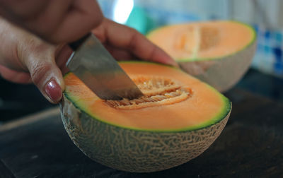 Cropped image of person cutting the cantaloupe 