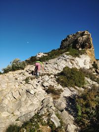 Low angle view of person on rock against clear blue sky