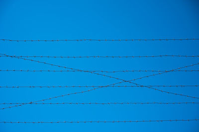 Low angle view of power lines against clear blue sky