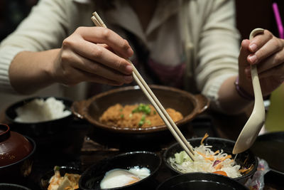 Close-up midsection of woman having meal with chopsticks at table