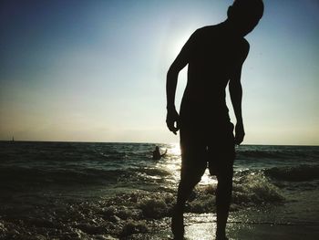 Silhouette man standing on beach against sky during sunset