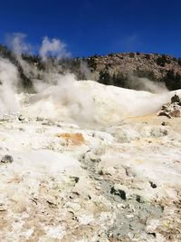 Steam emitting from volcanic landscape against clear blue sky