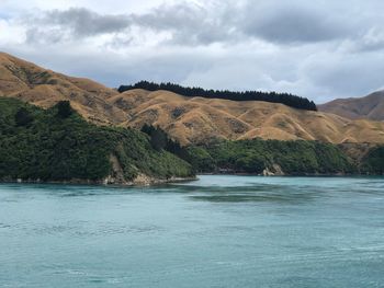 Scenic view of sea by mountain against sky