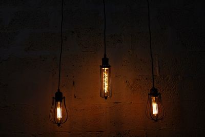 Low angle view of illuminated light bulb hanging on wall