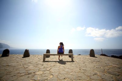 Rear view of woman sitting on beach against clear sky