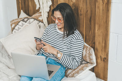 Girl at home on her bed uses laptop and phone