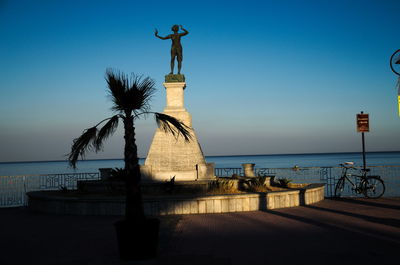 Statue in sea against clear blue sky