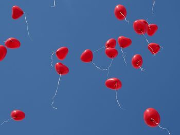Low angle view of red balloons flying against clear blue sky