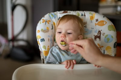 Baby girl sitting in high chair while her father feeding her