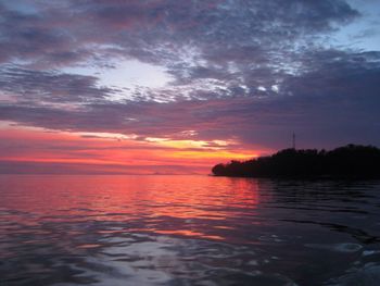 Scenic view of lake against cloudy sky at sunset