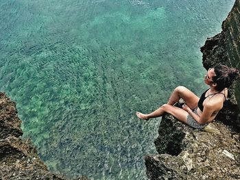 High angle view of woman sitting on cliff against sea