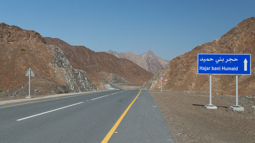 Road sign by mountains against clear sky