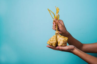 Midsection of person holding ketupat or rice pack in woven coconut leaves against blue background