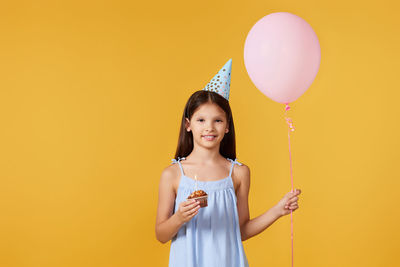 Portrait of young woman with balloons against yellow background