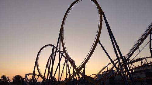 Low angle view of rollercoaster against sky at sunset